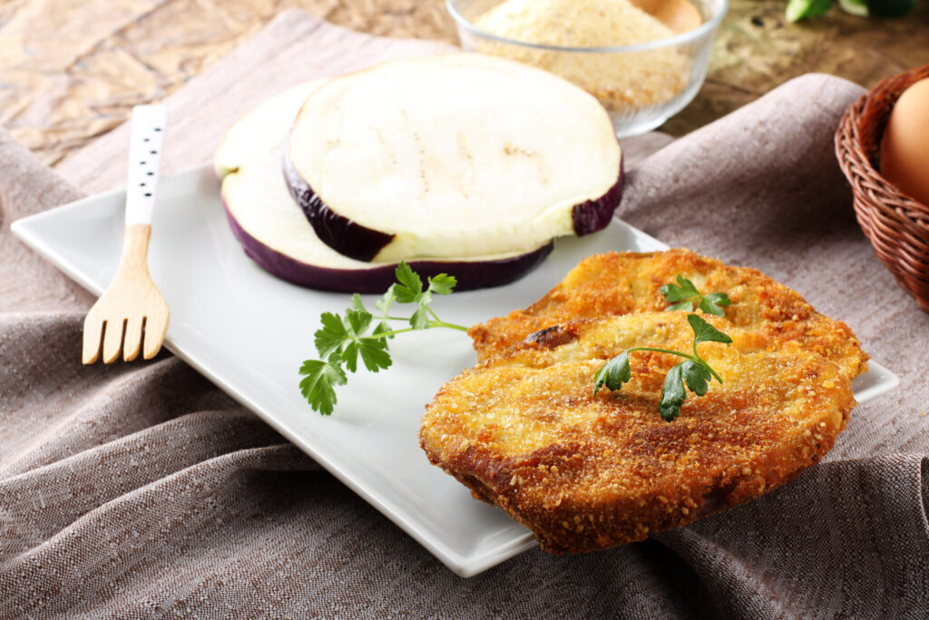 Eggplant cutlet with beaten egg and breadcrumbs on complex background