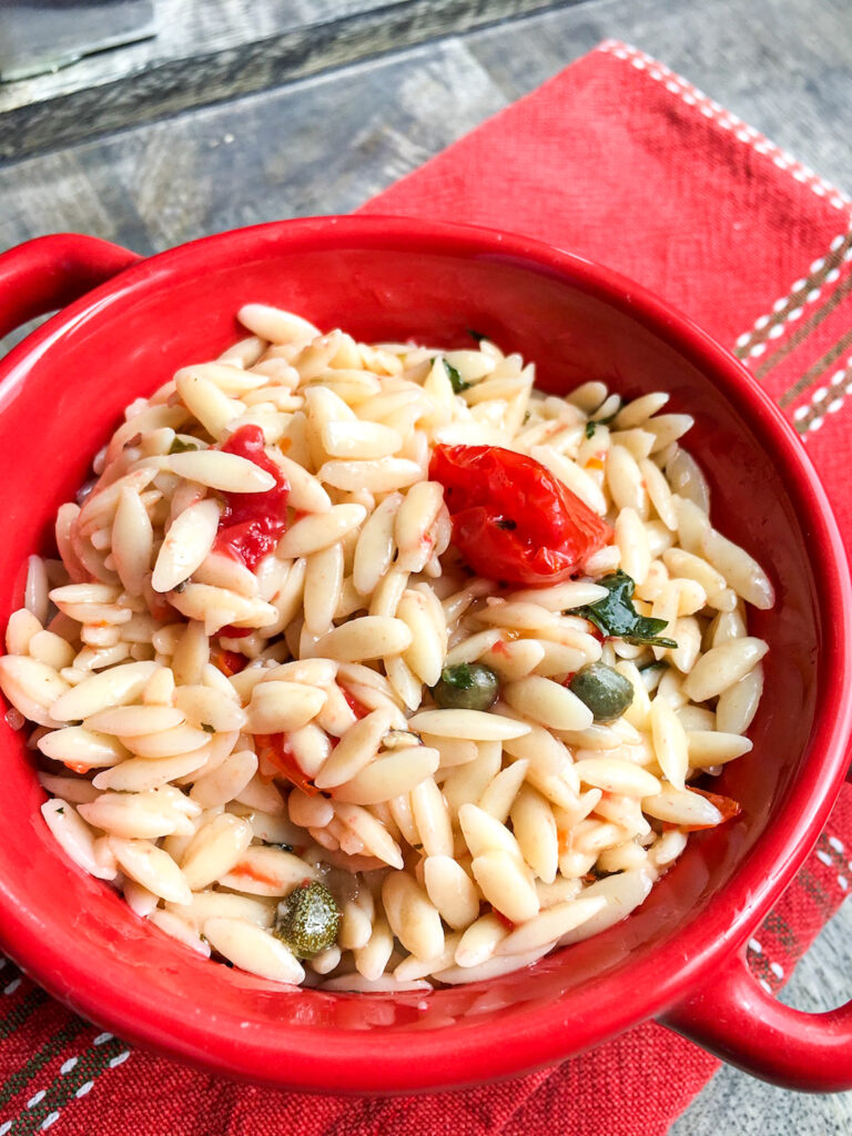 Healthy Orzo Pasta Salad with Tomatoes & Capers in red bowl on table
