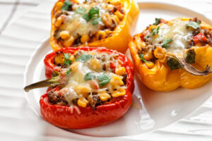 classic stuffed bell peppers with ground beef, corn and cheese on a white plate on a wooden table with golden cutlery, horizontal view from above