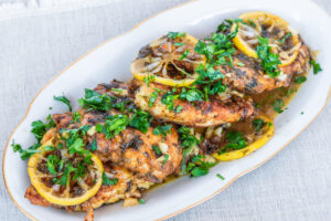 Chicken Piccata - slow cooker chicken breast with lemon slices and delicious sauce on a white plate close-up, top view