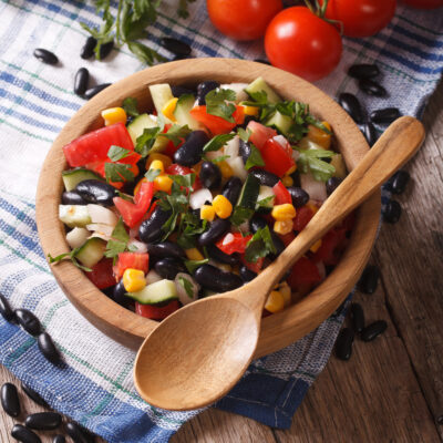 vegetable salad with black beans in a wooden bowl close-up and ingredients on the table. vertical