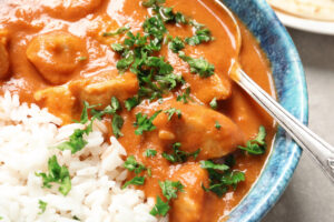 Delicious butter chicken with rice in bowl on table, closeup