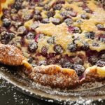Closeup of a freshly baked, rustic, homemade blueberry and lemon Dutch Baby puff pancake cooked in a cast iron skillet and dusted with icing sugar.