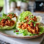 Honey sriracha rotisserie chicken lettuce cups with sesame seeds and green onions served on a plate for an easy high protein dinner recipe.
