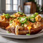 Jalapeño popper rotisserie chicken stuffed sweet potatoes topped with melted cheddar cheese and sliced jalapeños on a plate.